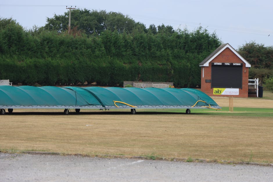 Image showing a row of four wooden outdoor rubbish bins positioned on a grassy area next to a hillside with trees in the background. The bins are constructed from vertical wooden slats with flat, over
